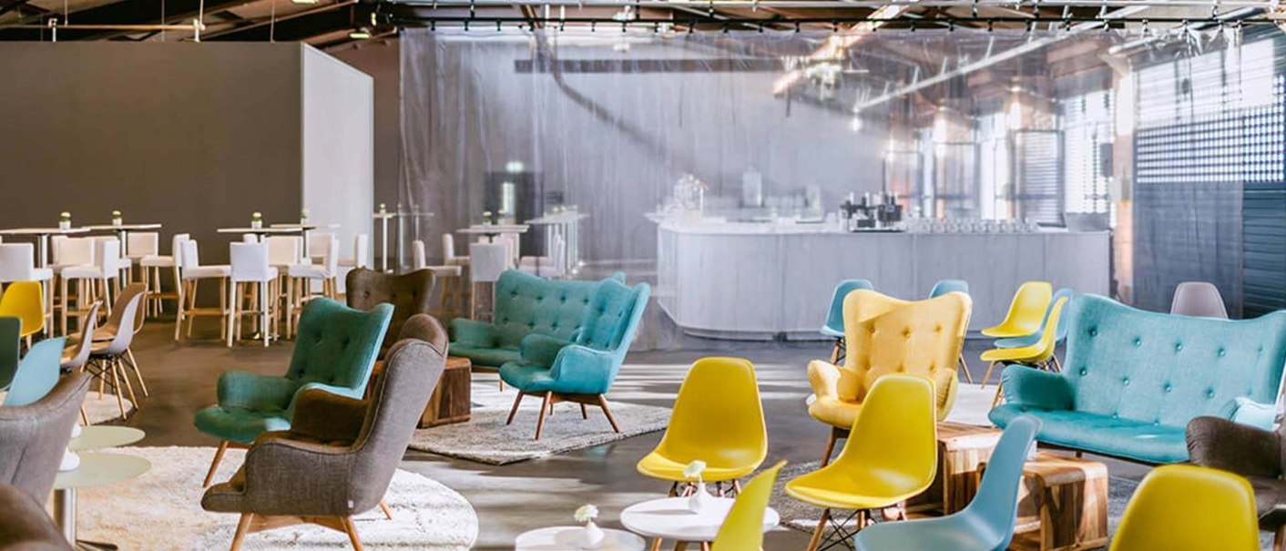 Modern function room with colorful armchairs and chairs, wooden beamed ceiling and bar in the background. Bright, inviting atmosphere., © rauschenbergercatering
