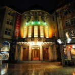 Eingang des Alten Schauspielhauses bei Nacht, beleuchtet mit bunten Lichtern. Die Fassade ist von historischen Gebäuden umgeben., © Schauspielbühnen Stuttgart