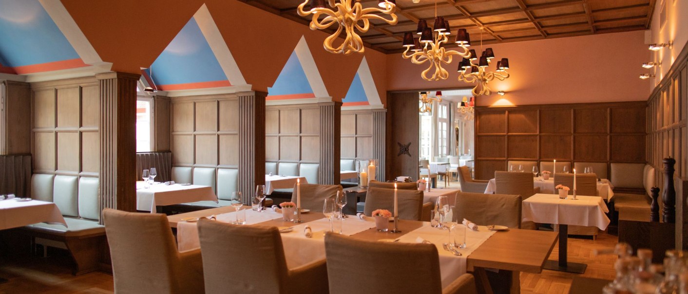 Elegant restaurant with laid tables, modern chandeliers and wooden walls. The ceiling is wood-panelled and the walls are painted in warm colors., © WHS Elegant restaurant with laid tables, modern chandeliers and wooden walls. The ceiling is wood-panelled and the walls are painted in warm colors., © WHS