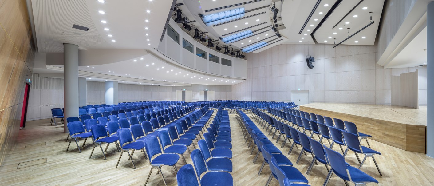 Moderner Saal mit blauen Stühlen, heller Holzverkleidung und Bühne. Deckenbeleuchtung und große Fenster sorgen für Helligkeit., © Kultur- und Kongresszentrum Liederhalle, Florian Selig Moderner Saal mit blauen Stühlen, heller Holzverkleidung und Bühne. Deckenbeleuchtung und große Fenster sorgen für Helligkeit., © Kultur- und Kongresszentrum Liederhalle, Florian Selig