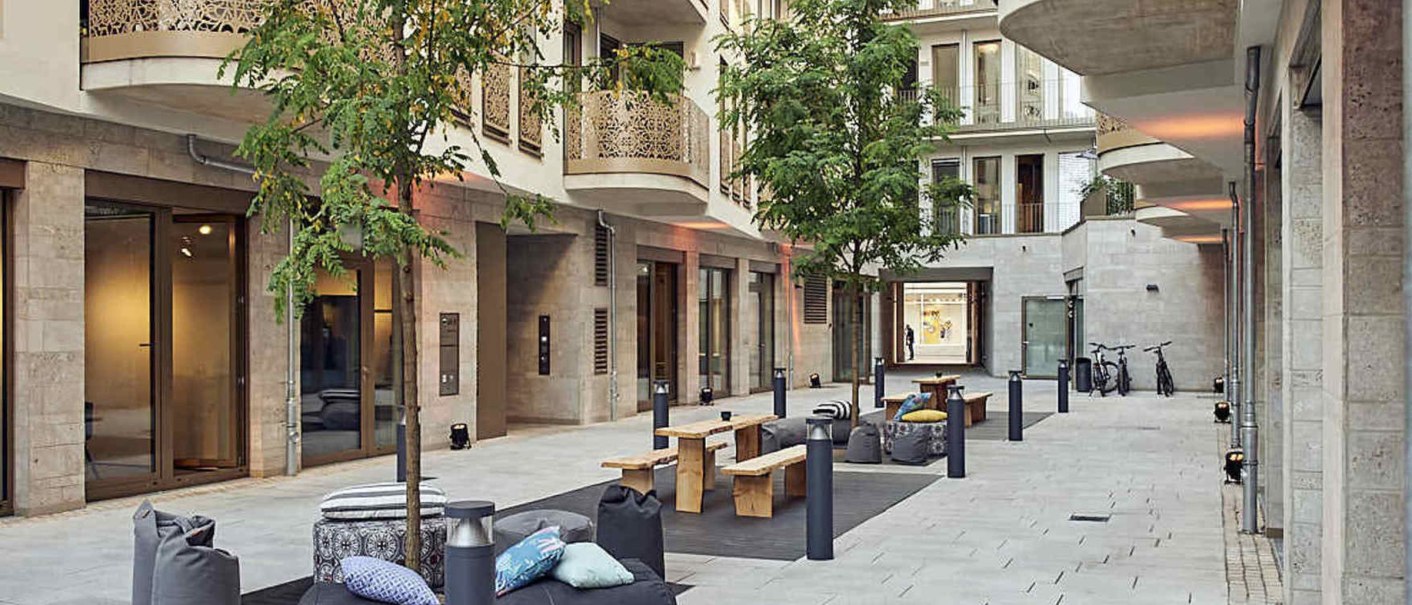 Modern courtyard with seating, trees and ornate balconies. Inviting atmosphere with wooden benches and cushions on beanbags., &copy; Design Offices
