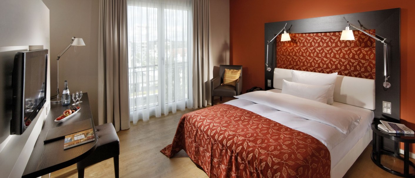 Stilvolles Hotelzimmer mit roter Bettdecke, Schreibtisch, Fernseher und Fenster mit Vorhängen., © Parkhotel Stuttgart Messe-Airport GmbH & Co KG Stilvolles Hotelzimmer mit roter Bettdecke, Schreibtisch, Fernseher und Fenster mit Vorhängen., © Parkhotel Stuttgart Messe-Airport GmbH & Co KG