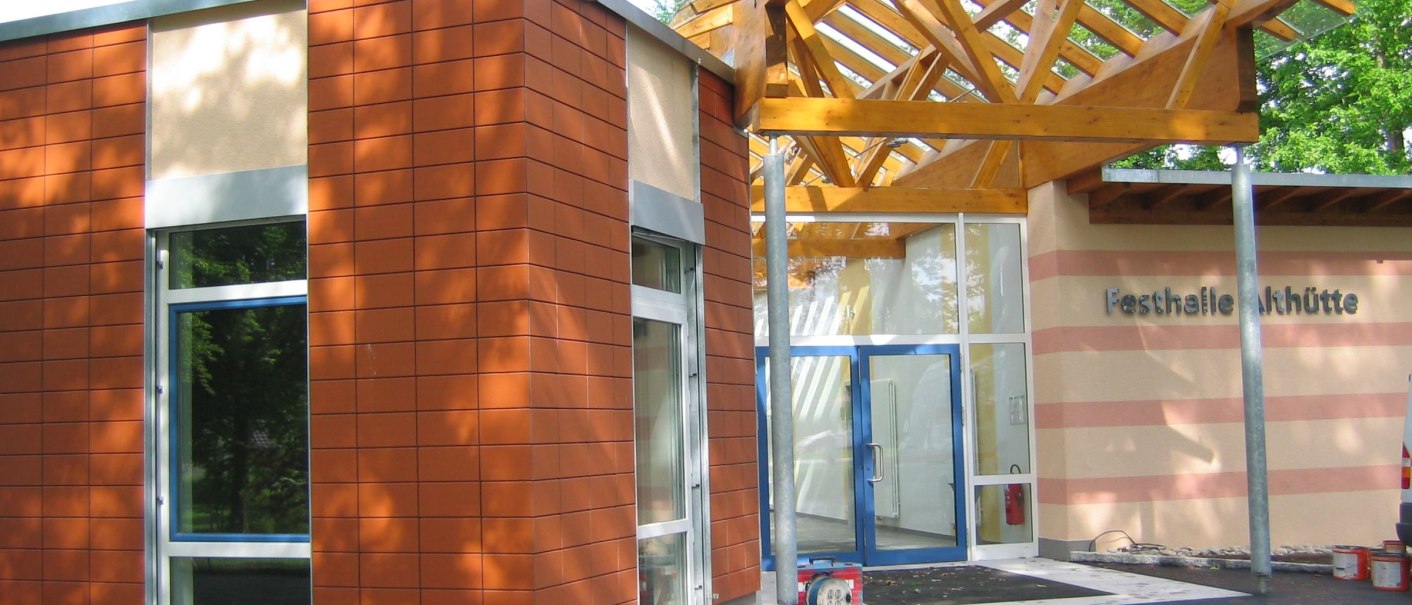 Moderner Eingangsbereich der Festhalle Althütte mit Glasfront und Holzdach. Die Fassade ist teils mit roten Kacheln verkleidet., © Gemeinde Althütte