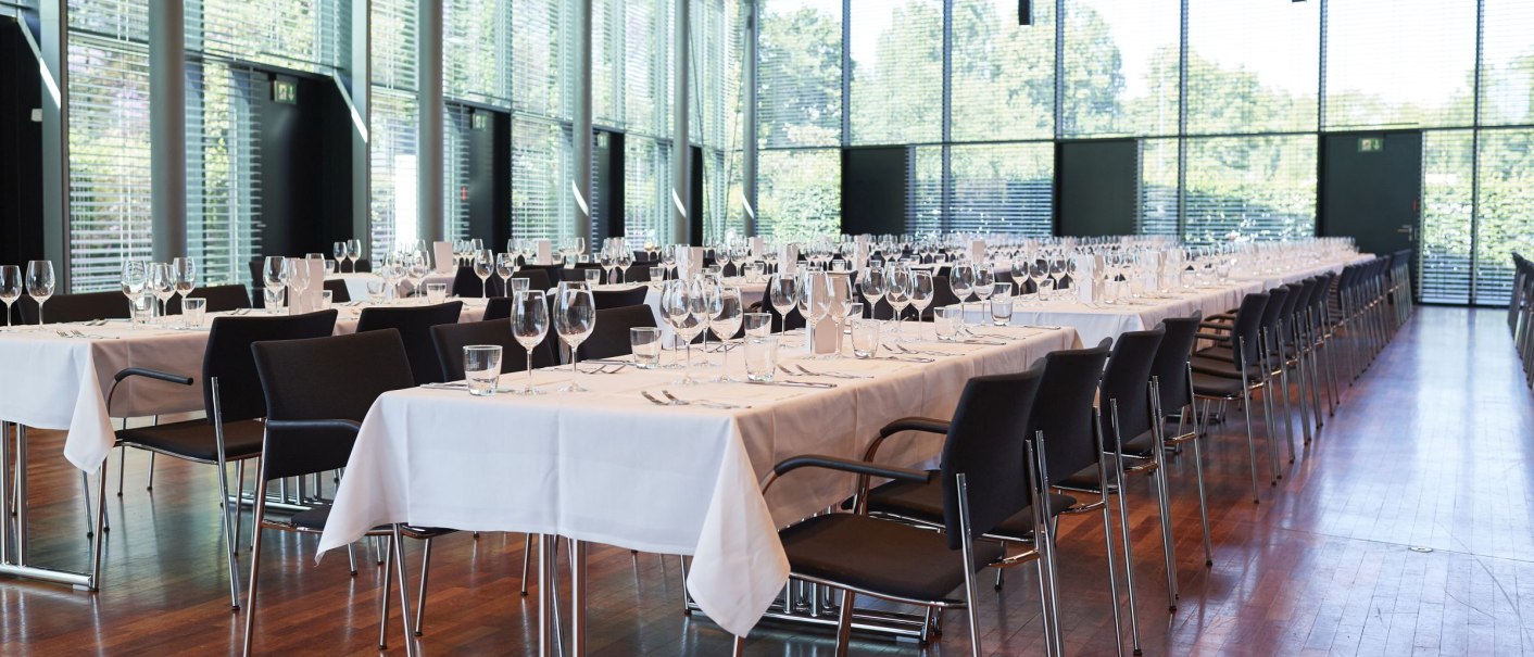 Moderner Veranstaltungsraum mit gedeckten Tischen, Stühlen und großen Fenstern. Perfekt für Events oder Bankette., © Peter Hartung