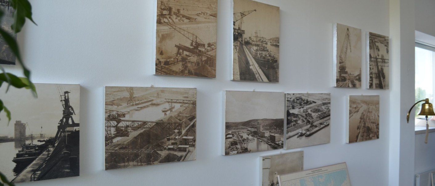 Mehrere historische Hafenfotos hängen an einer weißen Wand. Eine Pflanze und eine goldene Glocke sind im Vordergrund sichtbar., © Stuttgart-Marketing GmbH Mehrere historische Hafenfotos hängen an einer weißen Wand. Eine Pflanze und eine goldene Glocke sind im Vordergrund sichtbar., © Stuttgart-Marketing GmbH