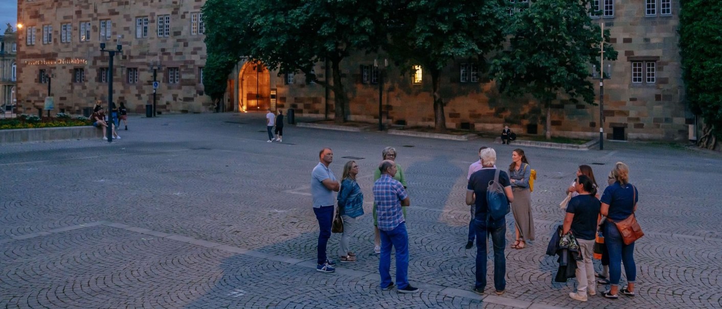Eine Gruppe von Menschen steht auf einem gepflasterten Platz vor einem historischen Geb&auml;ude bei D&auml;mmerung., &copy; Thomas Niederm&uuml;ller