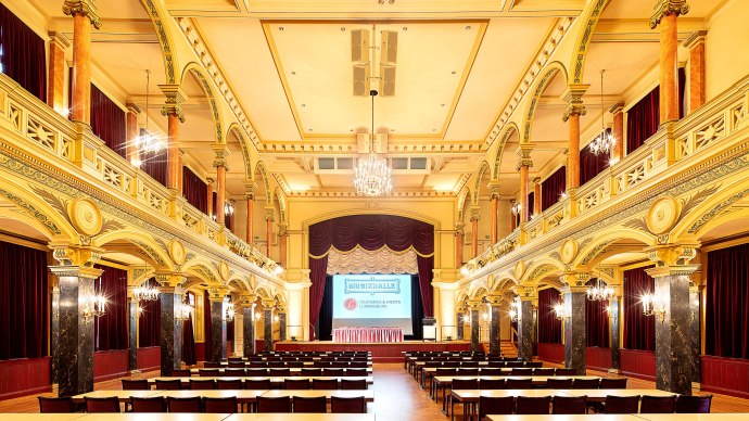 Prunkvoll verzierter Saal der Musikhalle Ludwigsburg mit Kronleuchtern, hohen Decken und Reihen von Tischen und Stühlen., © Stauch