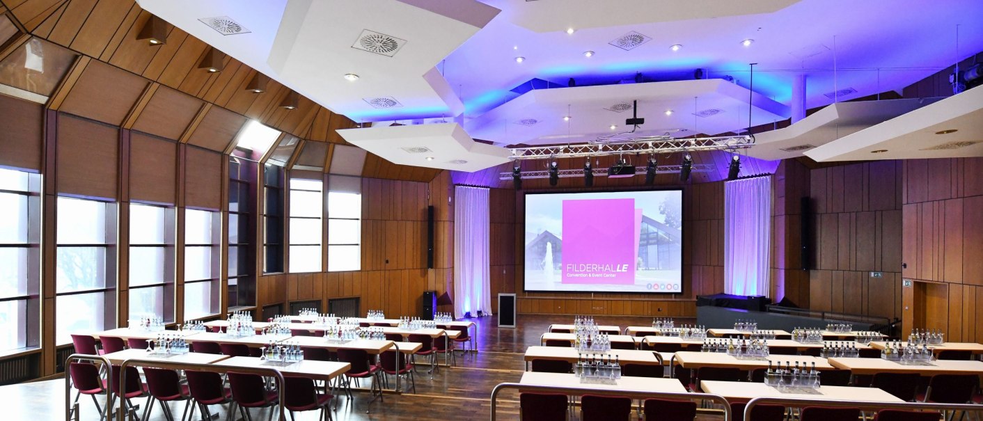 Moderner Konferenzraum mit Holzwänden, Tischen, Stühlen und einer großen Leinwand. Die Decke ist mit blauen Lichtern beleuchtet., © Guenter E. Bergmann - Photography