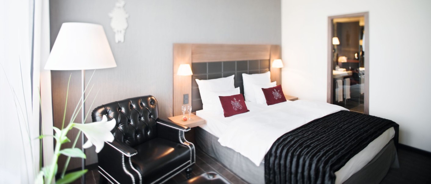 Elegantes Hotelzimmer mit Doppelbett, Ledersessel, Nachttischlampen und moderner Dekoration im Mövenpick Hotel Stuttgart Airport., © Mövenpick Hotel Stuttgart Airport