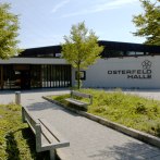 Die Osterfeldhalle von außen, umgeben von Bäumen und Pflanzen. Ein gepflasterter Weg führt zu Bänken vor dem Gebäude., © eslive