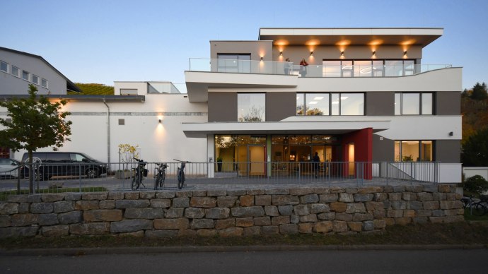 Moderne Geb&auml;udeau&szlig;enansicht mit Glasbalkonen, Beleuchtung und Fahrr&auml;dern im Vordergrund. Abendstimmung mit klarer, blauer Himmel., &copy; Architekurbuero-Gaysert