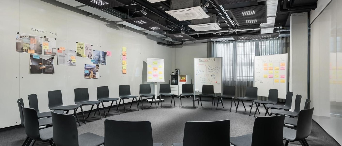 Moderner Schulungsraum mit Stuhlkreis, Whiteboards und Pinnwänden. Helle Beleuchtung und grauer Teppichboden schaffen eine professionelle Atmosphäre., © Design Offices GmbH