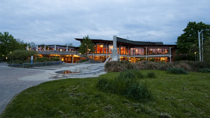 The Waiblingen community center at dusk, illuminated with large windows and surrounded by green spaces and sidewalks., © Peter Oppenländer The Waiblingen community center at dusk, illuminated with large windows and surrounded by green spaces and sidewalks., © Peter Oppenländer