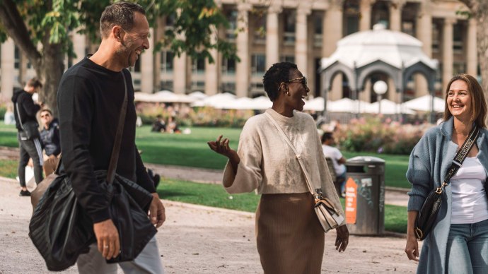 Drei Personen spazieren lachend im Oberen Schlossgarten. Im Hintergrund sind Bäume, ein Pavillon und ein Gebäude mit Säulen zu sehen., © SMG, wpsteinheisser