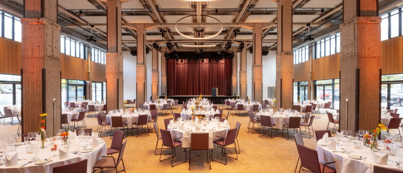 A large ballroom with round tables set in white, purple chairs and a stage. Modern lighting and high windows provide brightness., © Stefan Baraniecki A large ballroom with round tables set in white, purple chairs and a stage. Modern lighting and high windows provide brightness., © Stefan Baraniecki