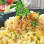 Käsespätzle mit Röstzwiebeln und Schnittlauch in einer Pfanne, daneben ein frischer Salat mit Tomaten und Gurken., © kab-vision - Fotolia