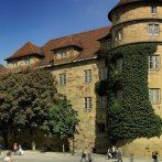 The Old Palace in Stuttgart with overgrown towers and trees in the foreground. People walking on the square in sunny weather., © Stuttgart-Marketing GmbH Florian Selig