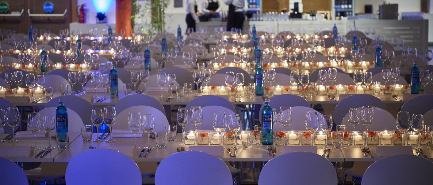Festlich gedeckter Saal mit weißen Stühlen, Gläsern und Kerzen auf den Tischen. Im Hintergrund stehen Personen an einer Bar., © PeterHartung Festlich gedeckter Saal mit weißen Stühlen, Gläsern und Kerzen auf den Tischen. Im Hintergrund stehen Personen an einer Bar., © PeterHartung