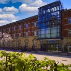 Das nestor Hotel Ludwigsburg zeigt eine Backsteinfassade mit moderner Glasfront. Blühende Bäume und blauer Himmel ergänzen die Szene., © nestor Hotel Ludwigsburg