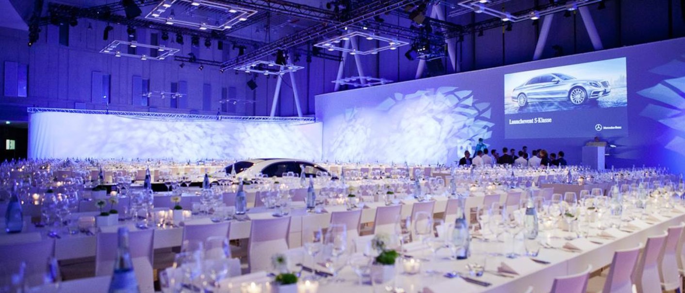 Elegant hall with laid tables for a launch event. A car is presented on a screen. The lighting is blue and atmospheric., &copy; Carl Benz Arena