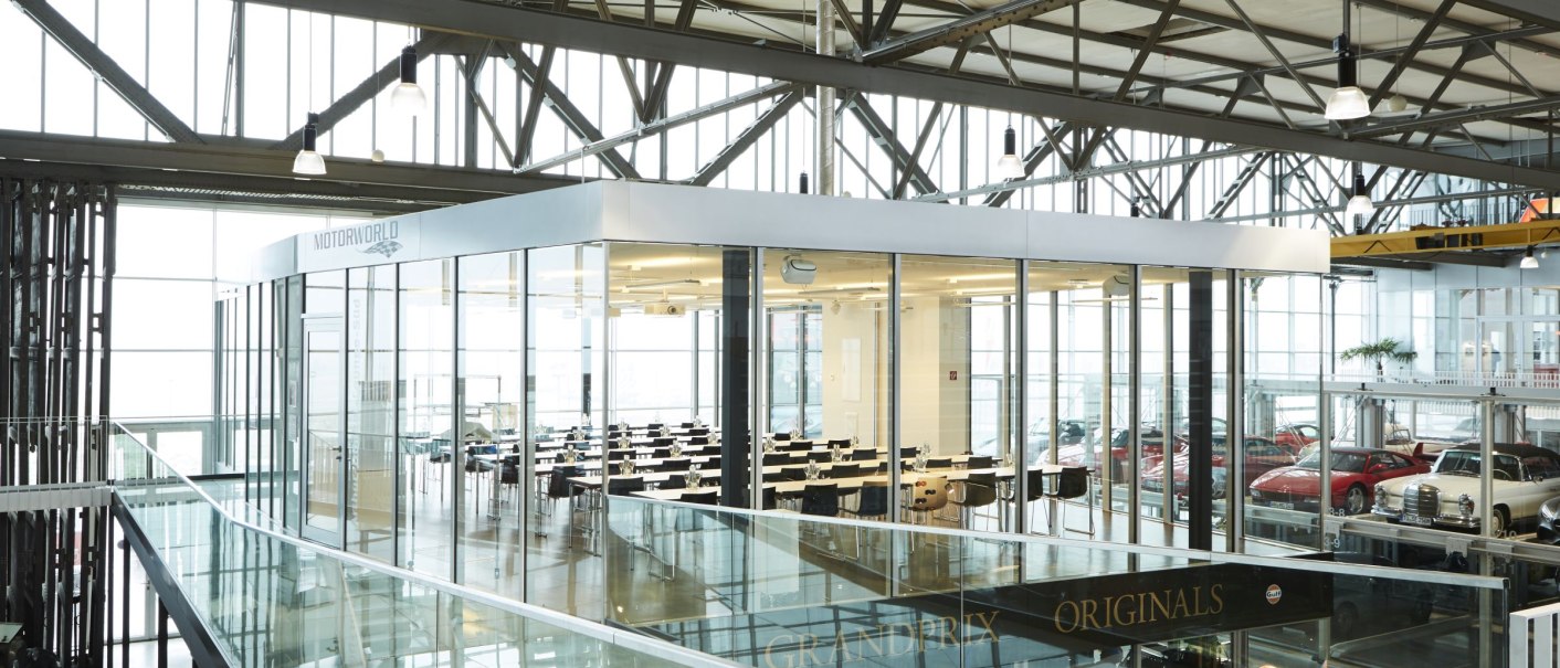 Interior view of Motorworld Region Stuttgart with modern glass walls, tables and classic cars in the background., &copy; MW Region Stuttgart