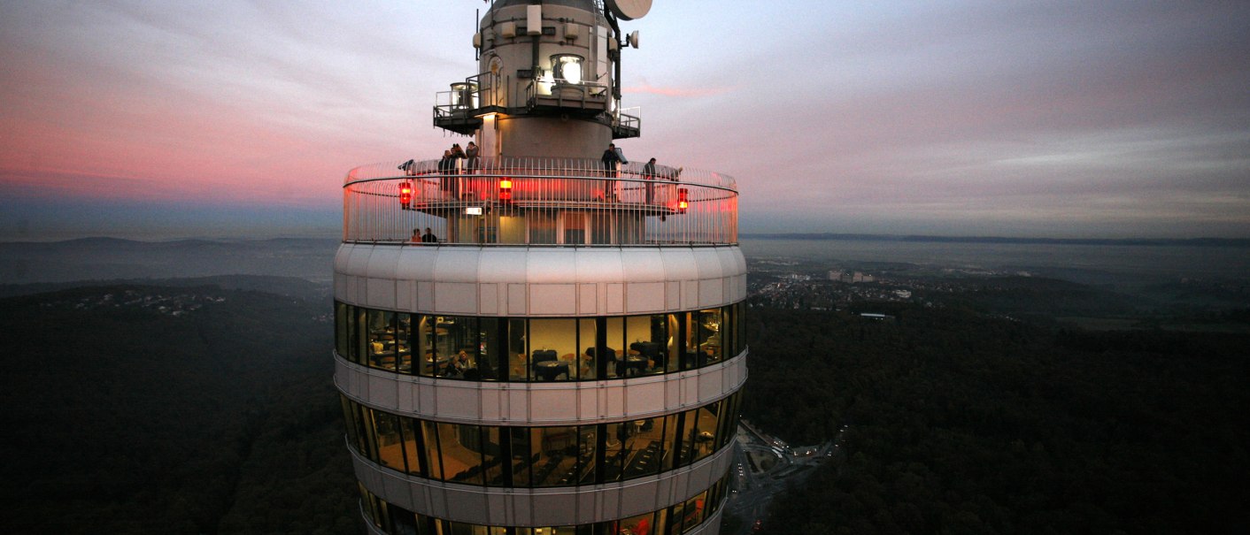 Ein Fernsehturm mit beleuchteter Aussichtsplattform bei Sonnenuntergang. Der Himmel ist rosa gefärbt, und die Landschaft erstreckt sich im Hintergrund., © SWR Media Services GmbH / Achim Mende