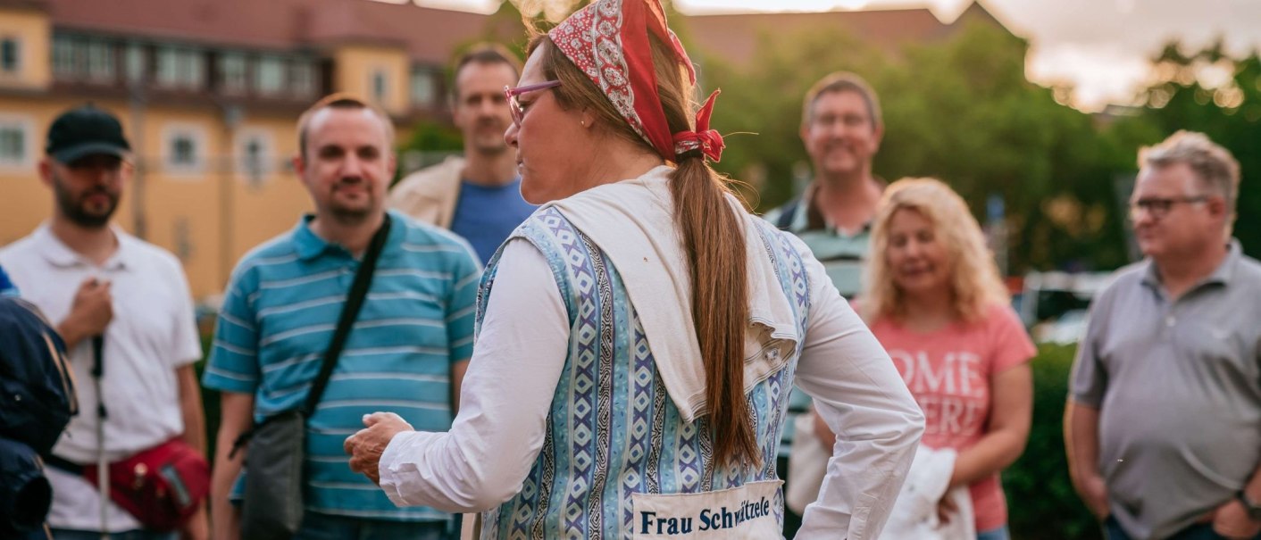 Eine Frau mit Kopftuch und Brille spricht zu einer Gruppe von Menschen im Freien. Sie trägt eine Weste mit der Aufschrift 'Frau Schwitzele'., © Thomas Niedermüller