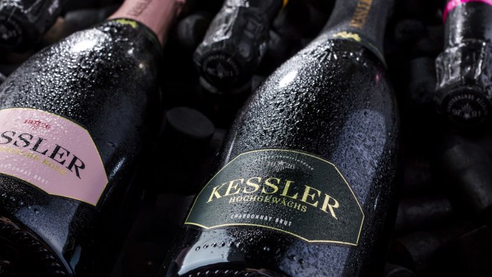Nahaufnahme von Kessler Sektflaschen, die mit Wassertropfen bedeckt sind. Die Etiketten zeigen verschiedene Sorten wie Rosé und Chardonnay Brut., © none Nahaufnahme von Kessler Sektflaschen, die mit Wassertropfen bedeckt sind. Die Etiketten zeigen verschiedene Sorten wie Rosé und Chardonnay Brut., © none