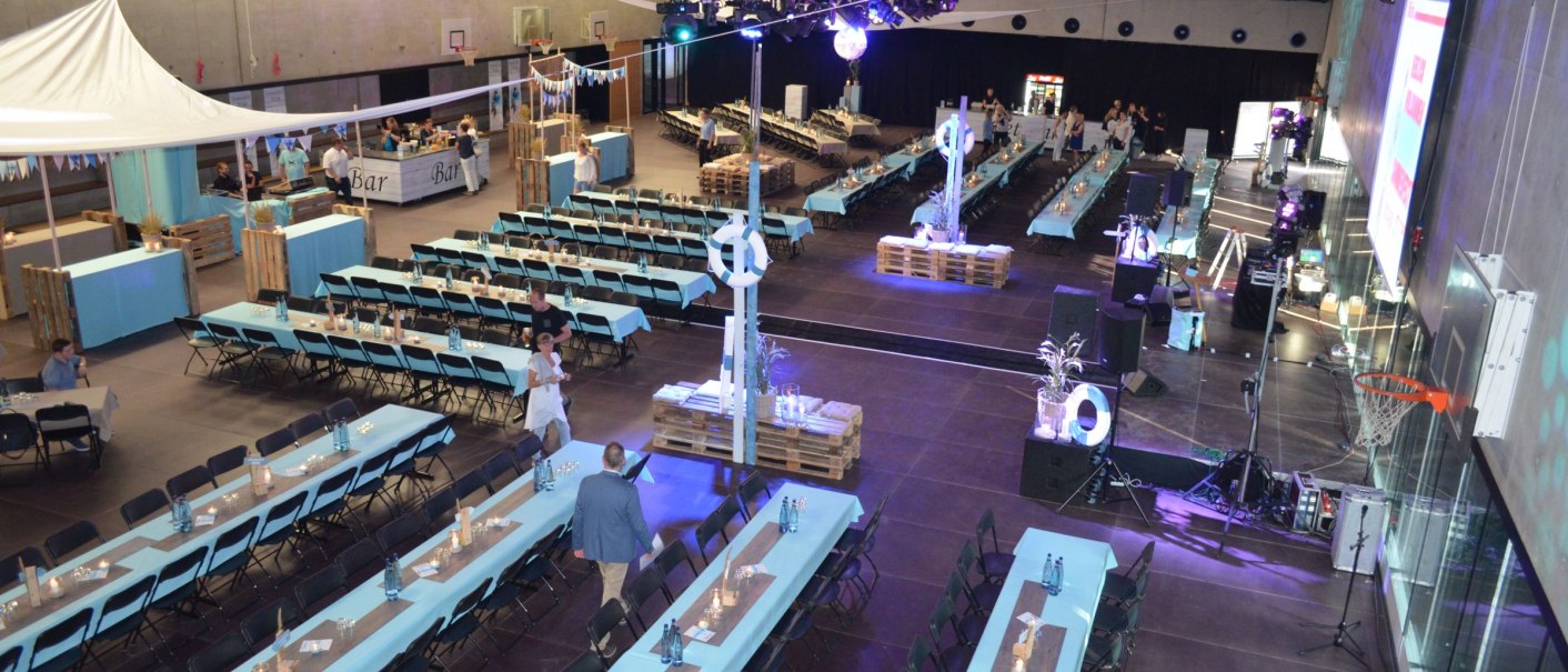 Large hall with long, set tables and chairs, decorated for a corporate event. Stage and bar in the background, subtle lighting., © EWS Arena Large hall with long, set tables and chairs, decorated for a corporate event. Stage and bar in the background, subtle lighting., © EWS Arena