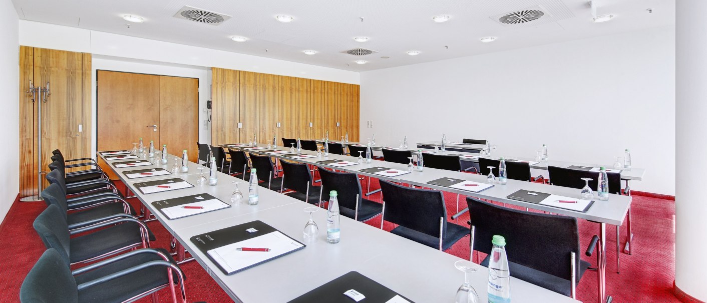 Ein heller Konferenzraum mit roten Teppichboden, Tischen und St&uuml;hlen. Auf den Tischen liegen Schreibunterlagen und Wasserflaschen., &copy; eslive_Martin Frey