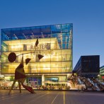 Das Kunstmuseum Stuttgart bei Abenddämmerung, beleuchtet mit moderner Skulptur im Vordergrund und Menschen auf der Treppe daneben., © SMG, Werner Dieterich