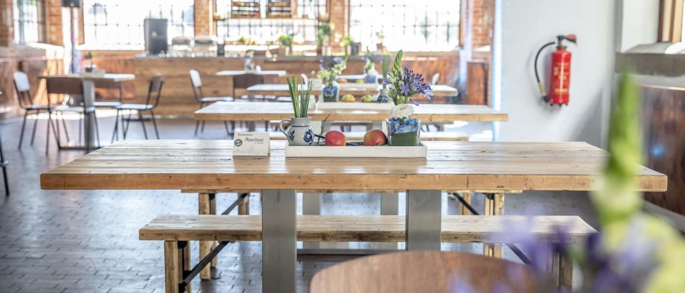 Bright foyer with wooden tables, floral decorations and large windows. Chairs and a fire extinguisher can be seen in the background., &copy; Exometa R&ouml;merkastell