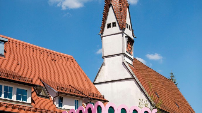 Bunt bemaltes Gebäude mit Drachenmotiv und pinken Details neben einer Kirche mit spitzem Turm in Plochingen., © Stuttgart-Marketing GmbH, Achim Mende