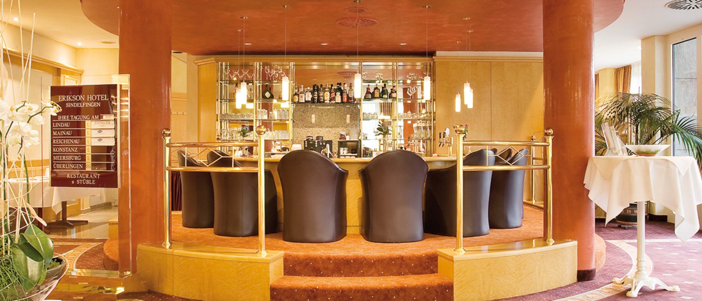 Elegante Hotelbar mit runden Säulen, Lederstühlen und gut bestücktem Regal. Warme Farben und stilvolle Einrichtung dominieren den Raum., © eriksonhotel_gf