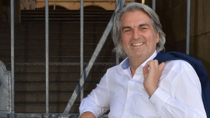 Ein Mann in weißem Hemd lehnt lächelnd an einem Gittertor. Im Hintergrund sind Treppen und ein historisches Gebäude zu sehen., © Wolfgang Seljé