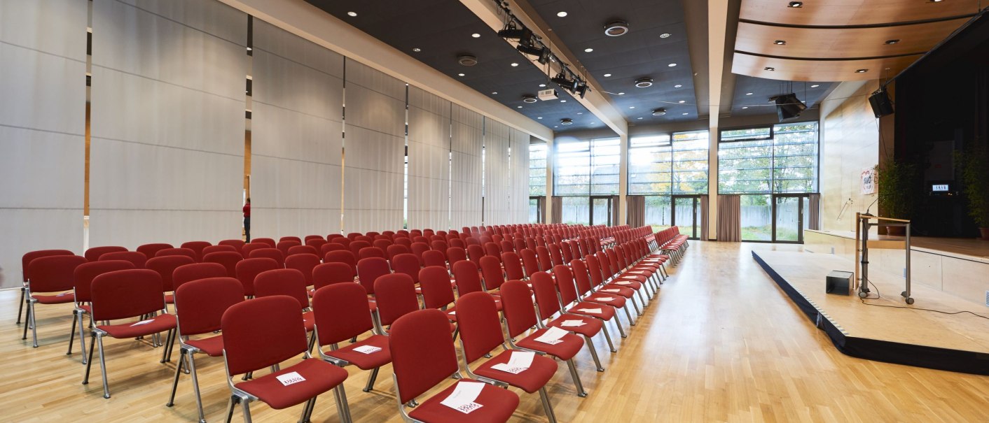 Interior view of the Schmiden festival hall with rows of red chairs, a stage and large windows. The room is modern and bright., &copy; bebopmedia lukas breusch