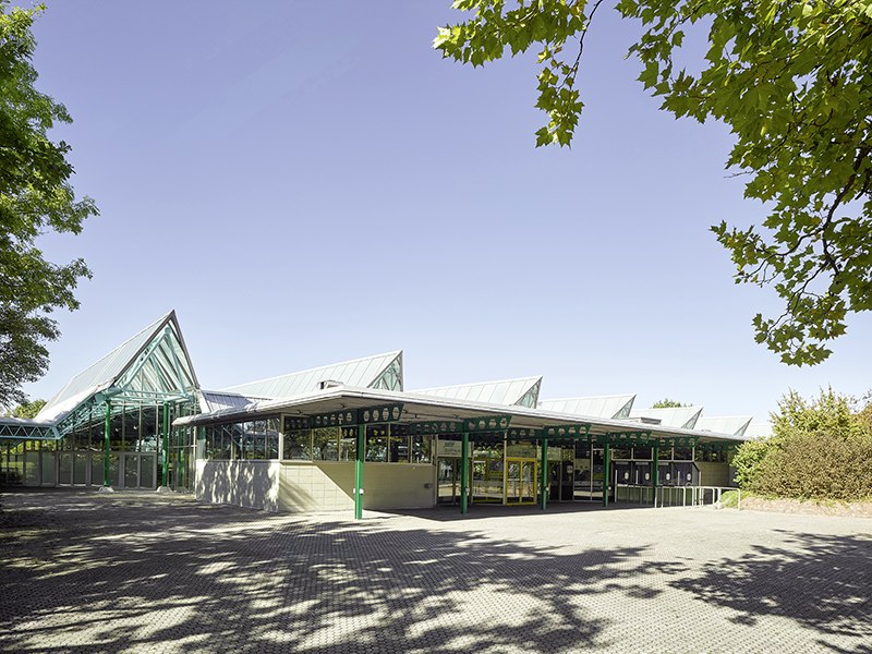 The Glaspalast Sindelfingen with its striking glass roof and green structures, surrounded by trees and a clear sky., &copy; Glaspalast Sindelfingen