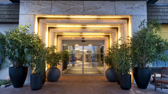 Modern hotel entrance with illuminated frame and revolving glass door, flanked by large plants in black pots., &copy; Wyndham Stuttgart Airport Messe