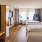 Modernes Hotelzimmer mit zwei Betten, Hängesessel, Tisch und Fernseher. Große Fenster mit Vorhängen lassen viel Licht herein., © Seminaris Hotels (Gerhard Hinz)