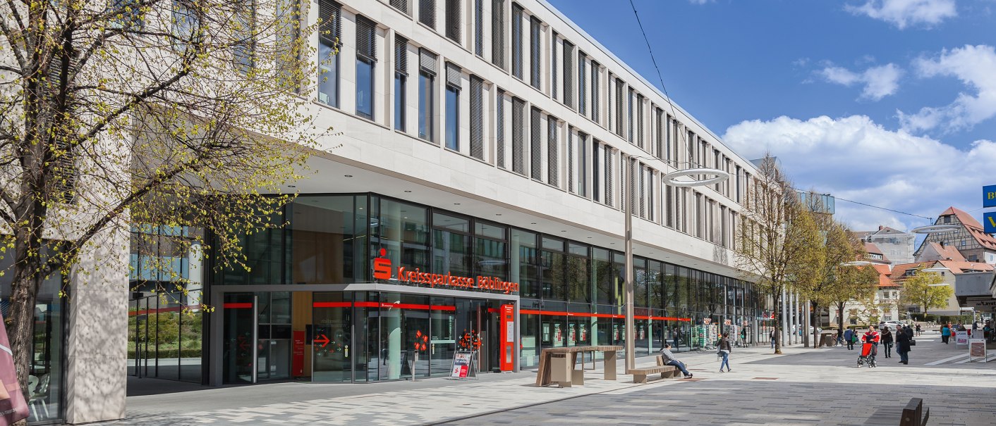The SparkassenForum Böblingen with its modern glass façade and pedestrian zone. People strolling in sunny weather. Trees with fresh leaves., © ccbs