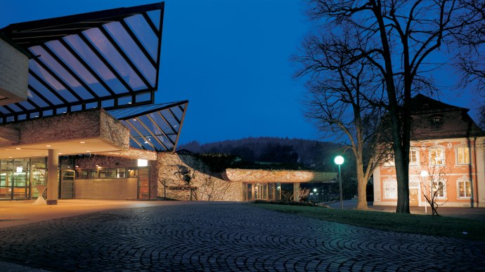 Modern architecture with glass roof at night, next to an illuminated historical building. Cobblestones in the foreground, trees in the background., &copy; Congress-Centrum Stadtgarten Schw&auml;bisch Gm&uuml;nd