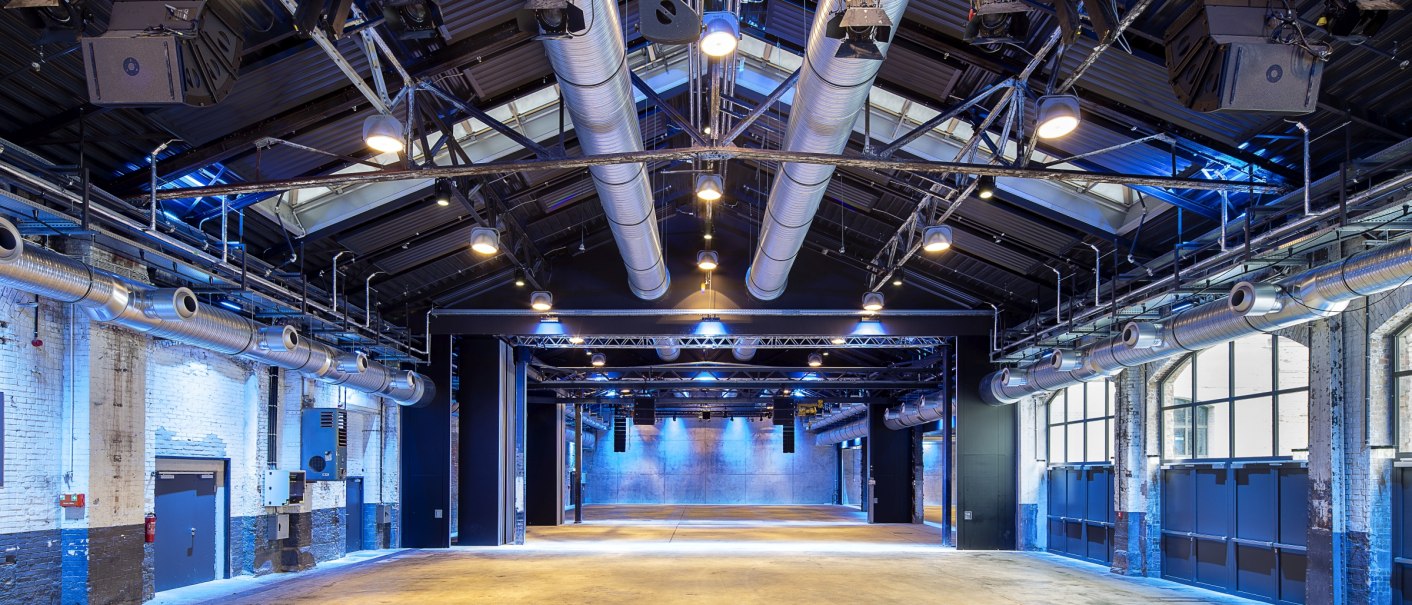 Große Halle mit industriellem Design, blauer Beleuchtung und sichtbaren Lüftungsrohren an der Decke. Die Wände sind aus Ziegeln, der Boden ist aus Beton., © Wagenhallen Stuttgart GmbH & Co. KG Große Halle mit industriellem Design, blauer Beleuchtung und sichtbaren Lüftungsrohren an der Decke. Die Wände sind aus Ziegeln, der Boden ist aus Beton., © Wagenhallen Stuttgart GmbH & Co. KG