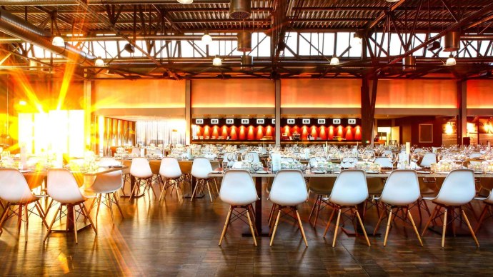 Ein gro&szlig;er Saal mit festlich gedeckten Tischen und wei&szlig;en St&uuml;hlen. Sonnenlicht str&ouml;mt durch die Fenster und beleuchtet den Raum warm., &copy; rauschenbergercatering