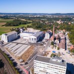 Aerial view of a factory with several buildings and a chimney, surrounded by fields and woods. Hills and a town can be seen in the background., © Stefan Baraniecki