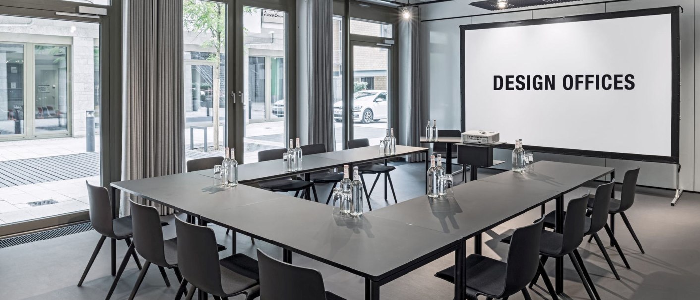 Modern conference room with U-shaped tables, chairs and a screen labeled 'Design Offices'. Large windows let in plenty of light., &copy; Design Offices