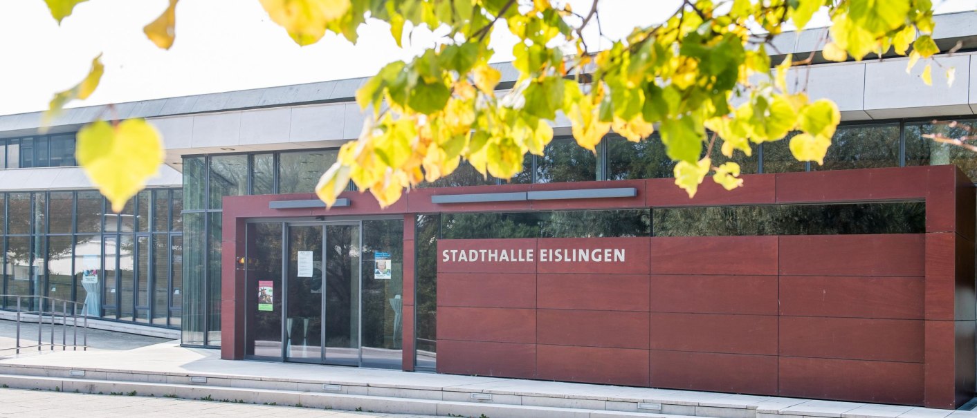 Die Stadthalle Eislingen mit moderner Glasfassade und rotem Eingangsbereich, umgeben von herbstlichen Blättern., © GIACINTO_CARLUCCI