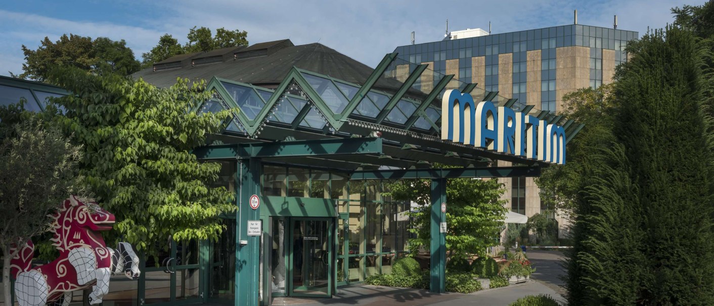 Exterior view of the Maritim Hotel Stuttgart with striking glass roof, surrounded by green trees and plants. A decorative horse stands on the left of the picture., © vision photos, Großbeerestr. 12b, 14482 Potsdam Exterior view of the Maritim Hotel Stuttgart with striking glass roof, surrounded by green trees and plants. A decorative horse stands on the left of the picture., © vision photos, Großbeerestr. 12b, 14482 Potsdam