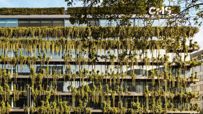 Ein modernes Geb&auml;ude mit einer &uuml;ppig begr&uuml;nten Fassade und gro&szlig;en Glasfenstern. Pflanzen h&auml;ngen von den Etagen herab., &copy; Stuttgart-Marketing GmbH, Sarah Schmid