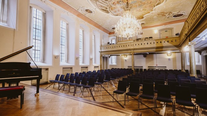 Eleganter Festsaal mit St&uuml;hlen, einem Fl&uuml;gel und einem pr&auml;chtigen Kronleuchter. Die Decke ist kunstvoll bemalt, und gro&szlig;e Fenster lassen viel Licht herein., &copy; NICO KURTH