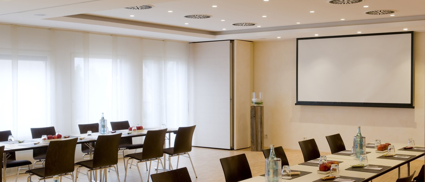 A modern meeting room with U-shaped tables, chairs, a presentation screen and drinks on the tables., &copy; Hotel Gloria
